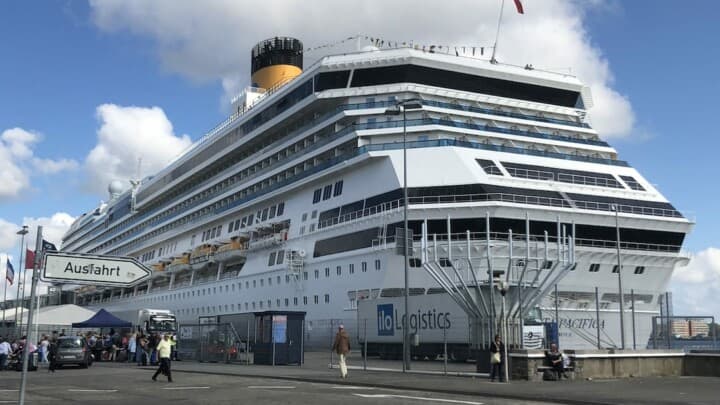 Unter blauem Himmel liegt der große Passagierschiff Costa Pacifica im Kieler Hafen. Im Kreuzfahrtterminal warten die Passagiere auf ihre Einschiffung.