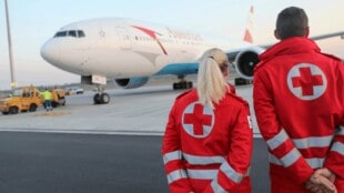 Zwei Mitarbeiter vom Österreichischen Roten Kreuz warten am Flughafen auf eine Lieferung mit Schutzausrüstung aus dem Ausland. Das Flugzeug ist bereits gelandet.