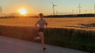 Eine Frau die gerade bei Sonnenuntergang läuft, im Hintergrund ist ein Feld zu sehen