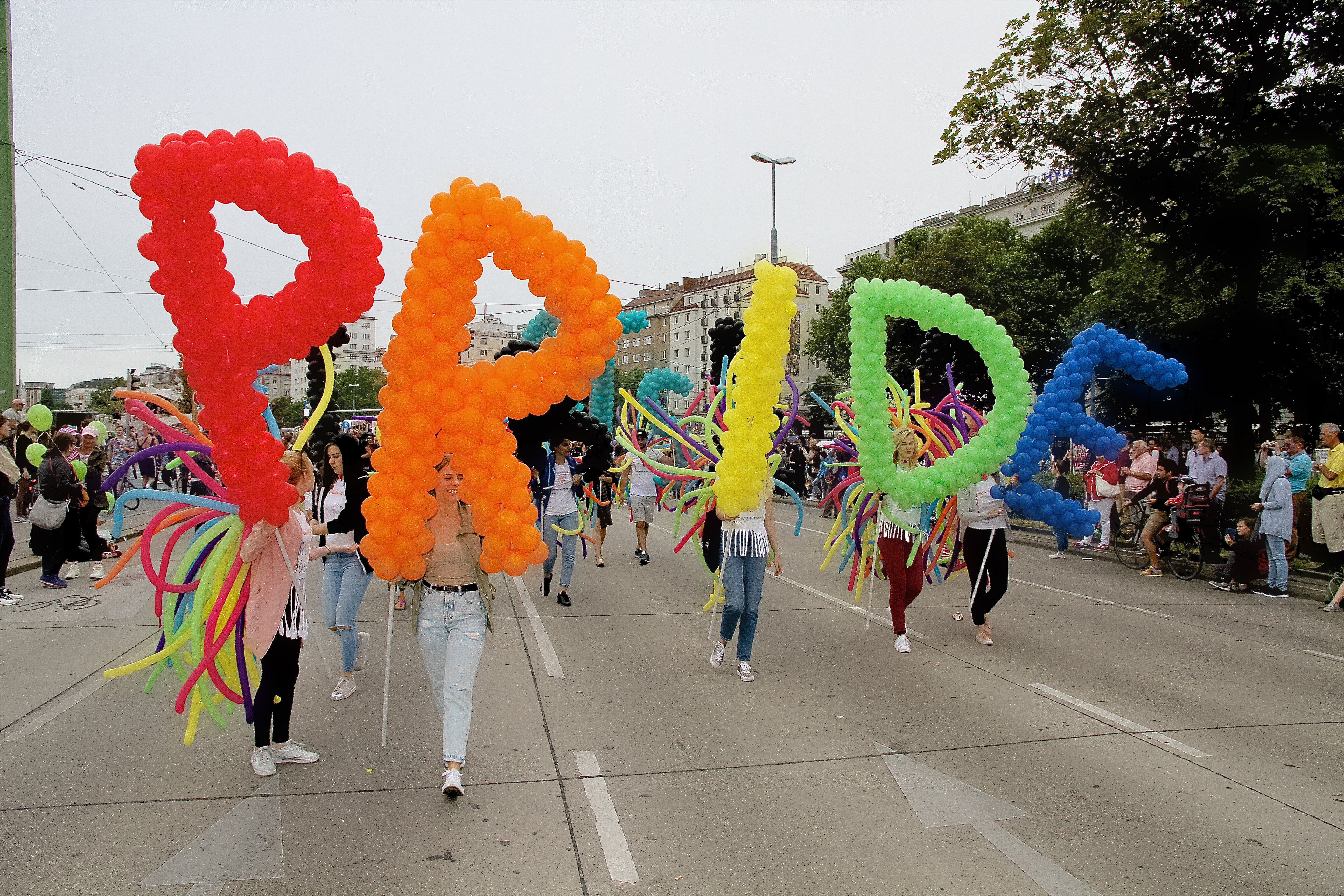 Regenbogenparade der Vienna Pride, viele Menschen demonstrieren auf der Straße und halten bunte Ballone in die Luft