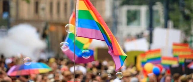 Regenbogenfahne die in einer großen Menschenmenge in die Luftgehalten wird, Vienna Pride in Wien, viele Menschen an der Regenbogenparade