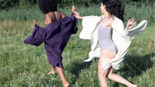 Zwei Frauen laufen verspielt in Unterwäsche und Robe über Wiese